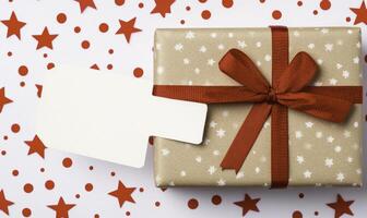 Gift wrapped in brown paper with red ribbon and white tag on white background photo