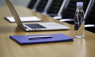 Modern office workspace with laptop, blue folder, pen, and water bottle on wooden table, showcasing minimalistic design for business and meetings photo