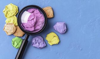 Colorful Crumpled Paper Balls with Magnifying Glass on Blue Background Representing Creativity and Investigation of Ideas and Concepts in Office Environment photo