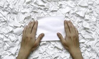 Blank White Sheet of Paper Being Held Above Piles of Crumpled White Paper Background Illustrating Concept of Fresh Ideas and Creativity in a Workspace photo