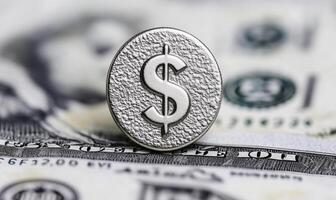 Silver dollar symbol on textured surface overlaid on US banknotes with blurred background highlighting concepts of finance, wealth, and currency transactions photo