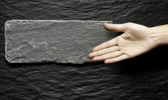 Hand Reaching Out to Touch a Textured Slate Surface Against a Dark Backdrop, Emphasizing Natural Materials and Simple Aesthetics in Interior Design photo