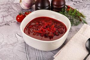 A bowl of red soup with a spoon and some vegetables photo