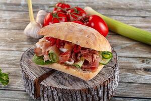 A sandwich on a wooden table with vegetables and tomatoes photo