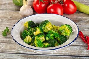 A bowl of broccoli and tomatoes on a wooden table photo