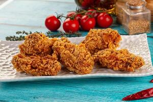 A plate of fried chicken on a table with tomatoes and spices photo