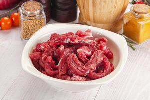 A bowl of raw meat sitting on a table next to a bottle of spices photo