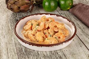 A bowl of shrimp and some lime slices on a wooden table photo