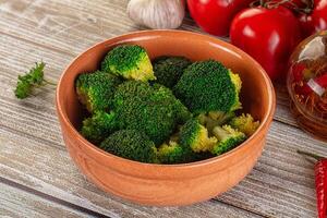 A bowl of broccoli with a bottle of olive oil and a bottle of red wine photo