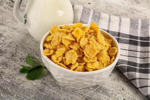 Corn flakes in a bowl next to a glass of milk photo