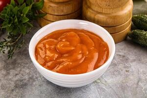 A bowl of tomato sauce next to a pepper grinder photo