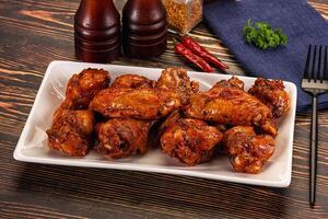 A plate of wings on a table with a bottle of beer and a fork photo