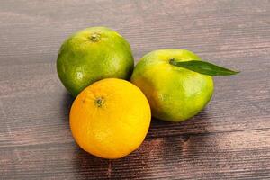 Three oranges and a lime on a wooden table photo