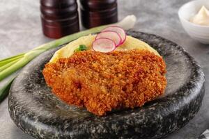 Fried chicken cutlet with pickles and onions on a stone plate photo