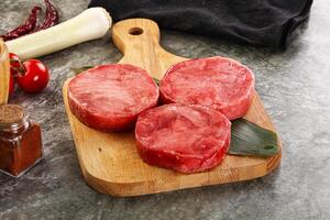 Three raw beef steaks on a cutting board with spices photo