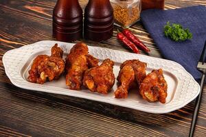 A plate of chicken wings on a table with a bottle of ketchup and a bottle of beer photo