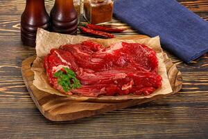 Raw beef on a cutting board with a bottle of beer and a bottle of hot sauce photo