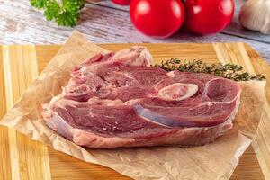A piece of meat on a cutting board with herbs and vegetables photo