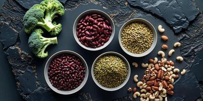 Overhead view of bowls filled with broccoli beans lentils and nuts on a dark textured surface photo