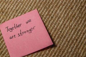 Together we are stronger written on a pink sticky note on carpet photo