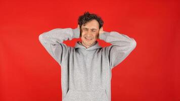 man covers ears with palms, does not want to listen to screams, loud music, avoids stress. Isolated on red background studio shot. concept - mental health, refusal to hear information. photo