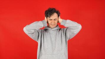 unhappy, angry, suffering man covers ears with palms, does not want to listen to screams, loud music, avoids stress. Isolated on red background of studio shot photo