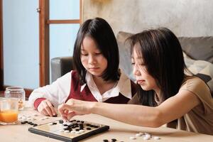 Asian family, mum, and kid cheerful playing Go, checkers board game on table in home living room together with love and fun, happy weekend relaxing hobby of child and parent, concentrate and compete. photo