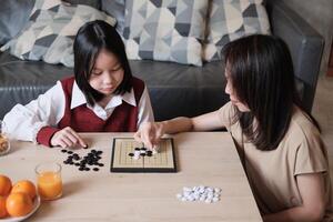Asian single mum, and child fun playing Go, checkers board game on table in home living room together with love and cheerful, happy weekend relaxing hobby of child and family, concentrate and compete. photo