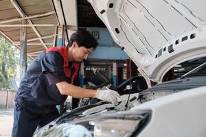 EV car check, Asian male mechanic worker inspects and maintains service of electric engine and battery in fixed automobile garage station, professional technology transportation industry business. photo