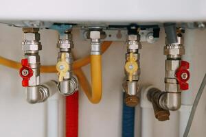 Close-up view of water heater pipes and valves in utility room, featuring colorful connectors and tubes. Essential components for heating system maintenance. Gas boiler taps. photo