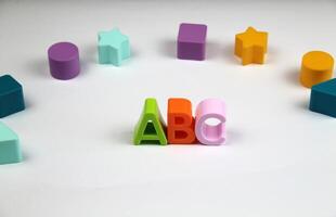 On a white background are bright and colorful letters of the English alphabet, in the background are figures of different shapes. concept of learning photo