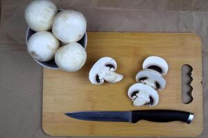 There are mushrooms on the plate, a knife and slices of champignons are on the board next to it photo