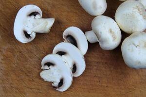 Sliced mushrooms lie on a wooden board, in the background are whole large champignons photo