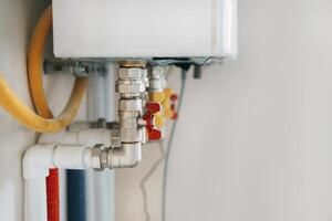view of water heater pipes and valves in a utility room, featuring colorful connectors and tubes. Essential components for heating system maintenance and operation. Gas boiler taps. photo