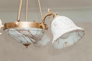 Image of vintage chandelier with ornate marble shades, captured in a broken state. The delicate design features elaborate metalwork and intricate artistry, highlighting its antique charm. photo