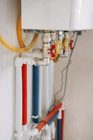 Installation of gas boiler with colored pipes equipped with valves and connectors for efficient supply of hot and cold water in the residential water supply system photo