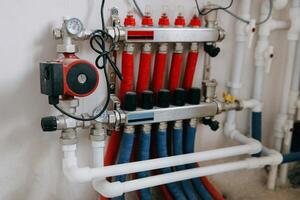 Central heating system image showing multiple red and blue pipes connected to control panel with valves and gauges. System is set up against plain wall. Underfloor heating photo