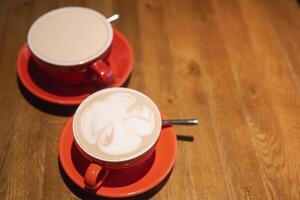 Artistic latte creations served in red cups on wooden table. A perfect representation of a cozy cafe atmosphere for coffee lovers photo