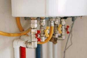 Close-up view of water heater pipes and valves in a utility room, featuring colorful connectors and tubes. Essential components for heating system maintenance and operation. Gas boiler photo