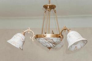 Image of a vintage chandelier with ornate marble shades, captured in a broken state. The delicate design features elaborate metalwork and intricate artistry, highlighting its antique charm. photo