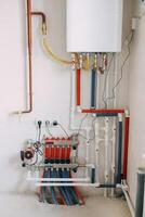Detailed view of an intricate heating system setup featuring red and blue color-coded pipes, valves, and gauges. Connection diagram of a gas boiler with a underfloor heating system photo