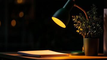 A desk lamp is on a table with a book and plant photo