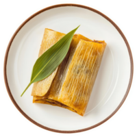 Golden tamale resting on a plate with a decorative leaf. png