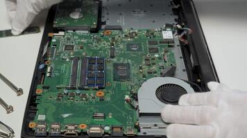 A technician is carefully replacing components on a laptop motherboard while wearing protective gloves in a tidy, well-lit workspace filled with tools. video