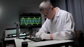 A technician works diligently on a circuit board in a well-equipped lab. A monitor displays a waveform, highlighting the precision of electronics repair. video