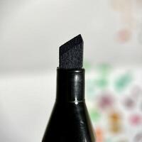 Close up black chisel shaped stationary nib isolated on square paper surface background. photo