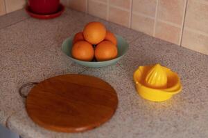 On the table are a plate of oranges, a cutting board, and a citrus juicer photo