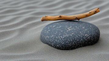 A smooth stone with a stick on sandy surface. photo