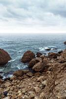 Scenic rocky coastline under overcast sky with waves crashing against stones photo
