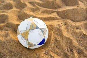 Worn soccer ball resting on sandy beach during bright daylight hours in a recreational setting photo